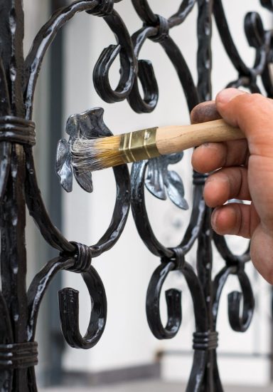 Contractor's hand with brush that painting metal fence.